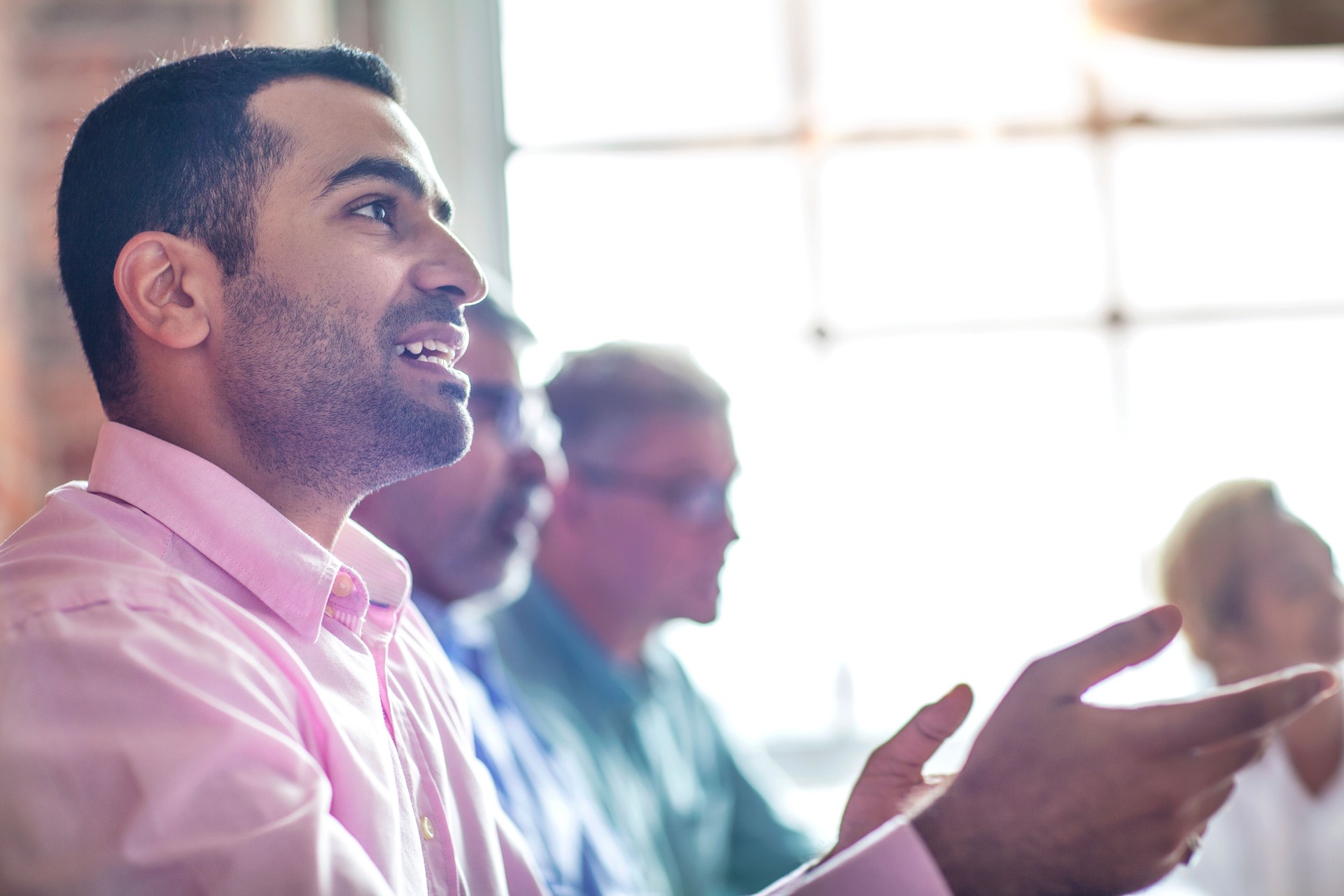 Asian Indian mid adult man smiling talking with office colleagues during business meeting