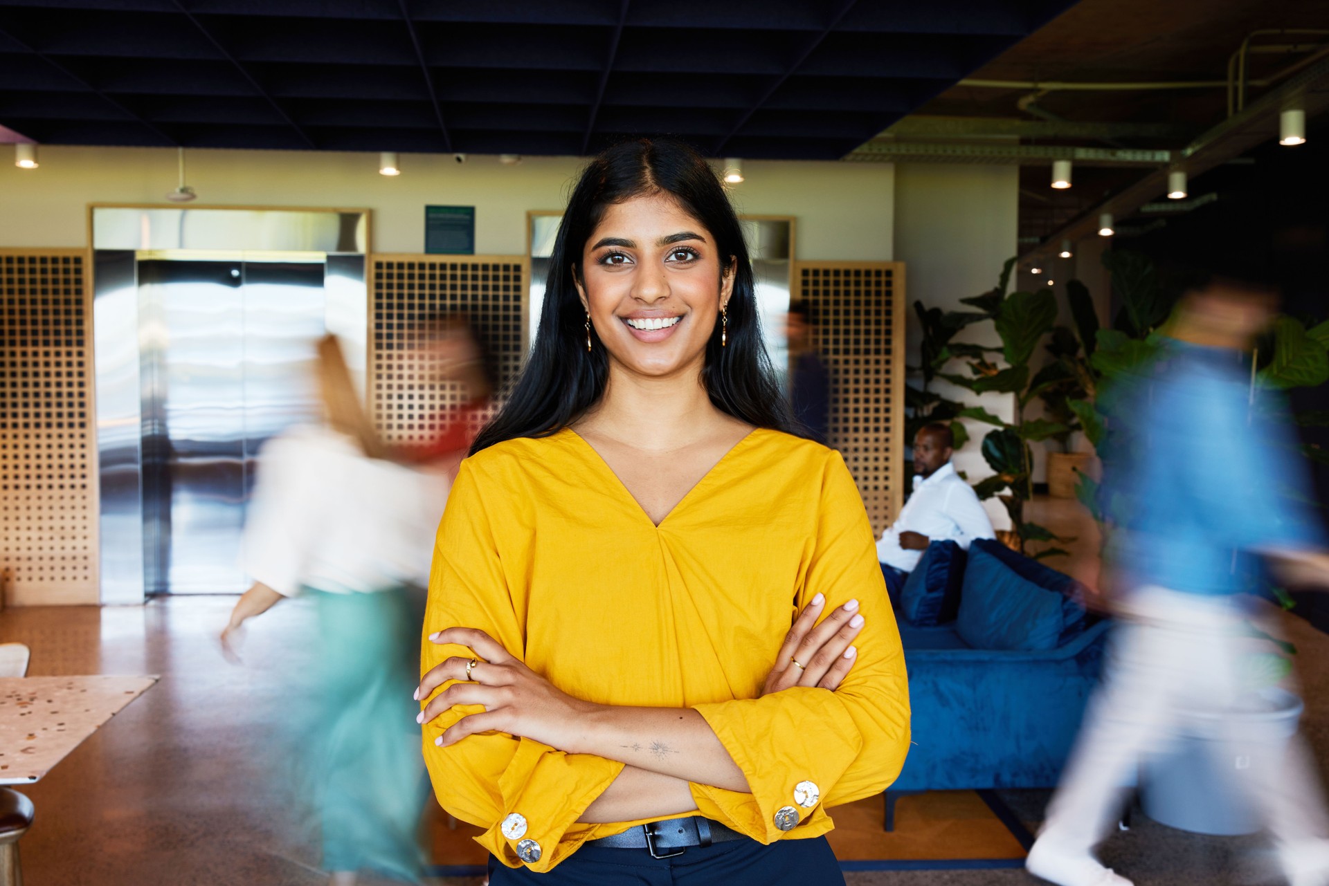 Young businesswoman smiling in an office with blurred coworkers walking behind her
