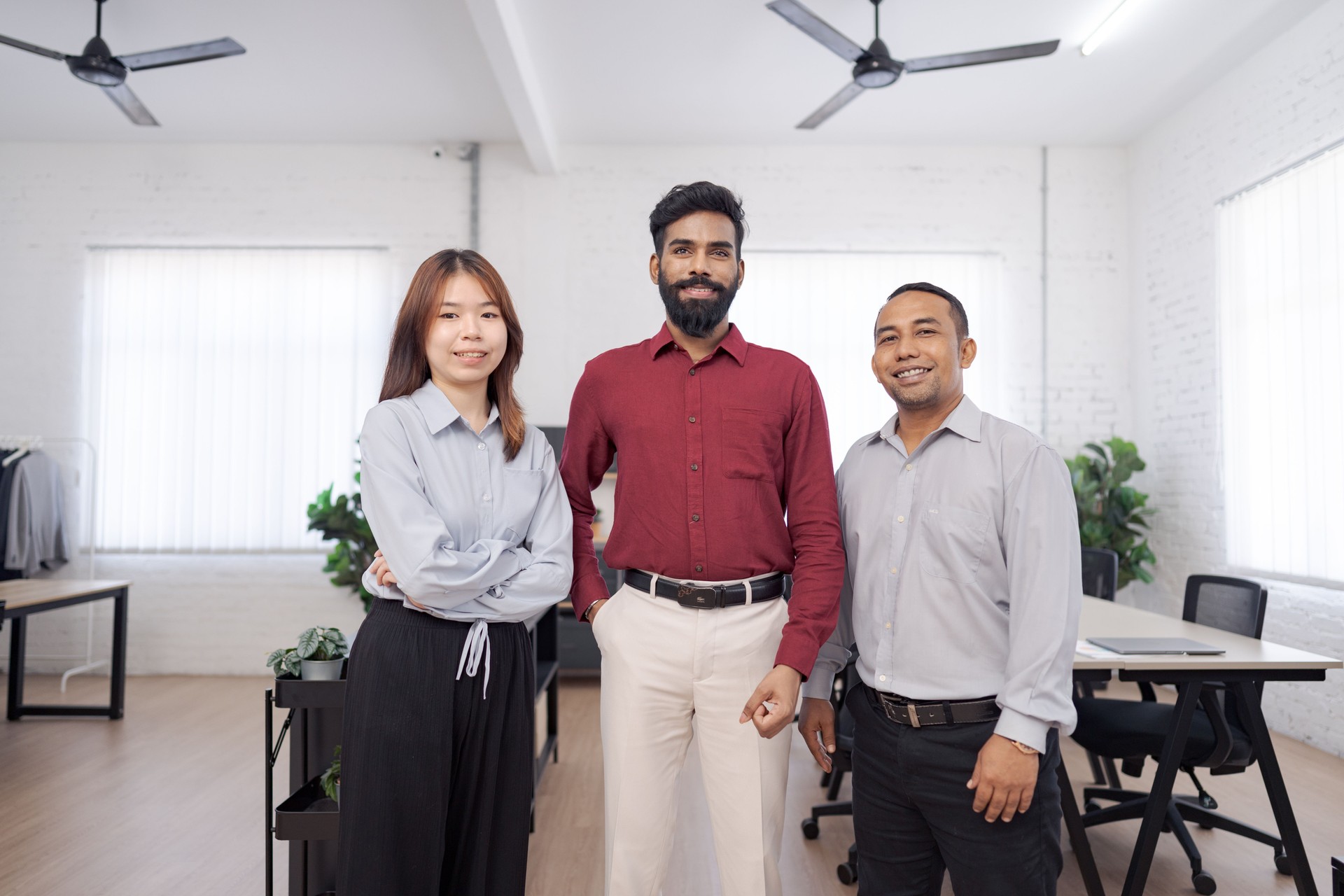 Diverse team of four young professionals standing confidently in modern open office with arms crossed, showcasing teamwork